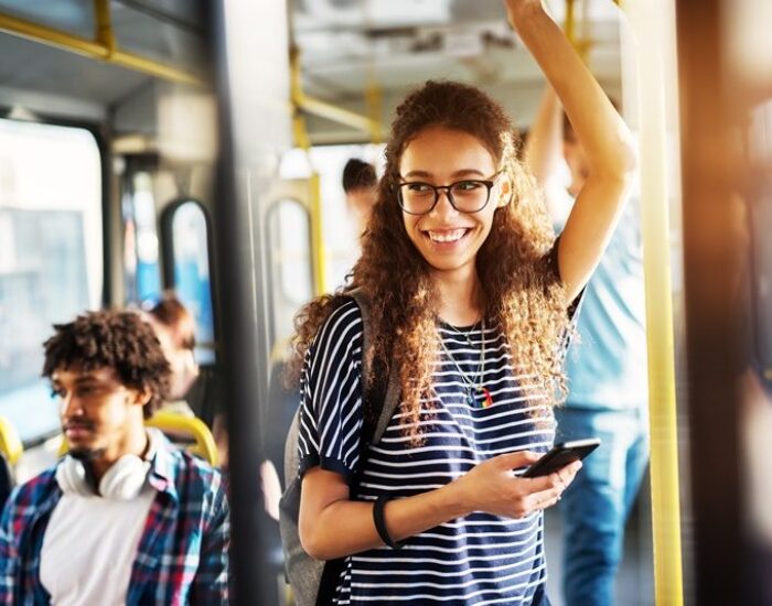 Young gorgeous cheerful woman is standing on the bus using the phone and smiling.